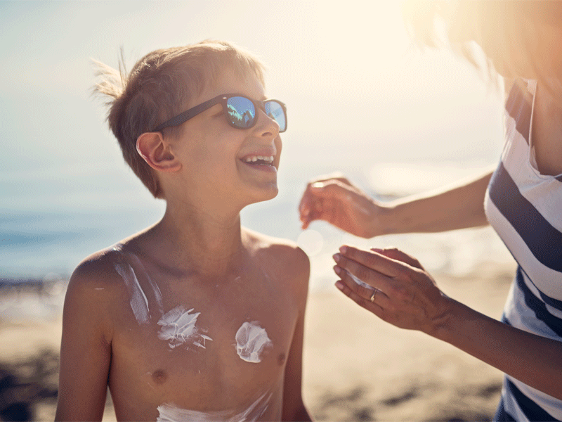 Kind wird von seiner Mutter mit Sonnencreme eingeschmiert